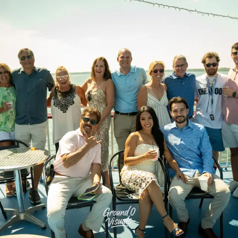 Group of people smiling on a boat deck under sunny skies.