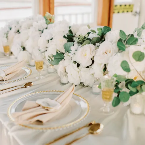 Elegant table setting with white flowers, greenery, and gold-rimmed plates.