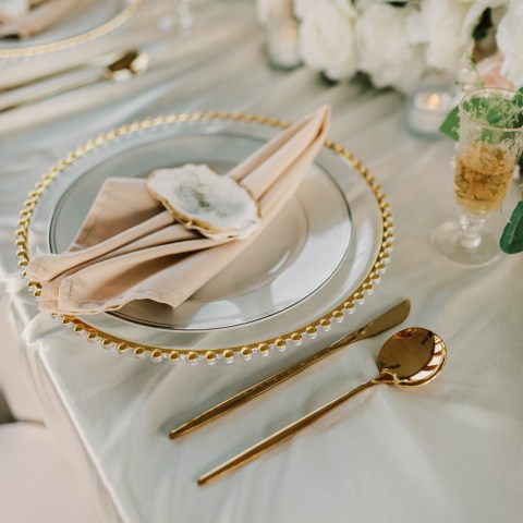 Elegant dining setup with gold cutlery, ivory napkin, and floral centerpiece.