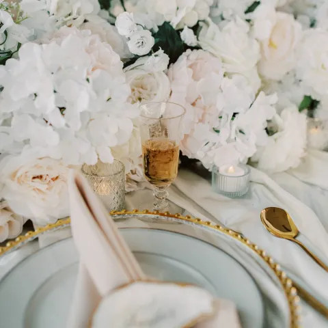Elegant table setting with white flowers, plate, napkin, and candle.