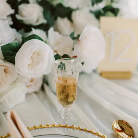 Elegant table setting with flowers, a numbered card, and a glass of champagne.