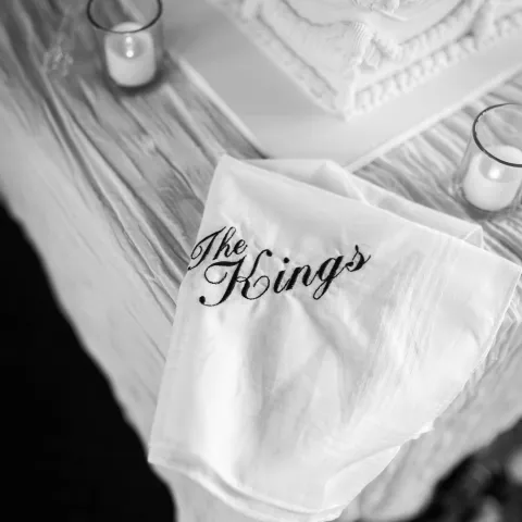 Black and white photo of a cake with 'The King's' napkin and small candles.