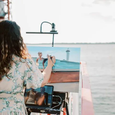 Person painting a seascape on a canvas near water.