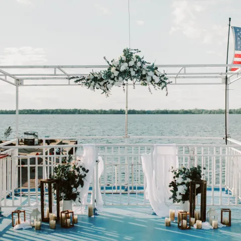 Outdoor wedding altar by the lake with floral arch and chairs on a blue deck.
