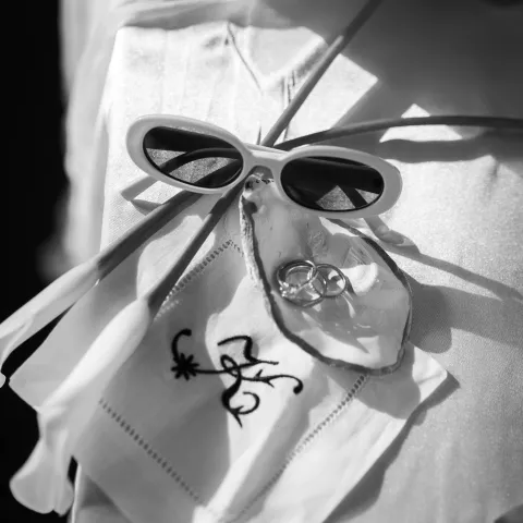 Black and white photo of sunglasses, rings in a shell, and a monogrammed cloth.