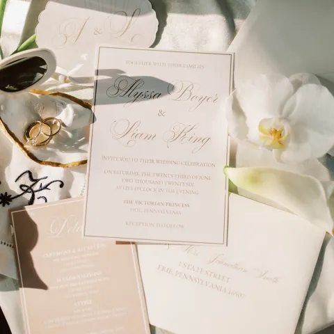 Elegant wedding invitations with gold rings and white orchid on silk fabric.