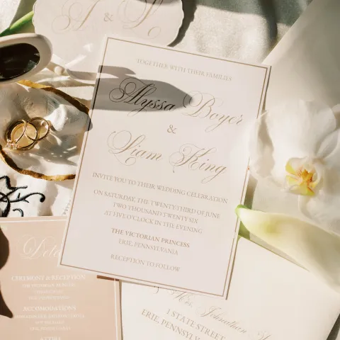 Wedding invitation set with rings and white flowers on a satin background.