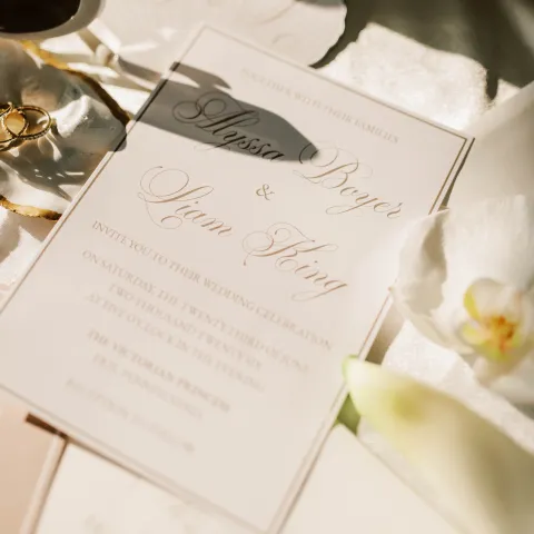 Elegant wedding invitation with rings and flowers in soft light.