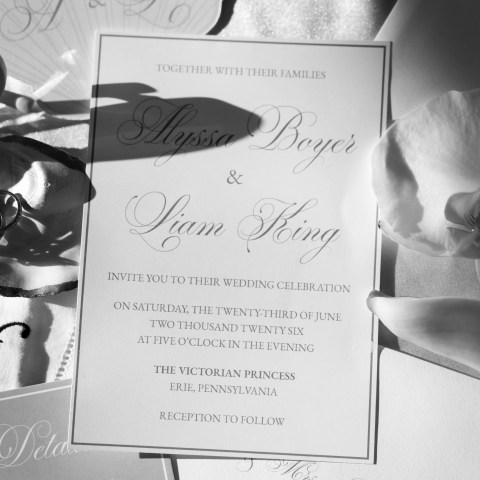 Wedding invitation with elegant script and floral accents in grayscale.