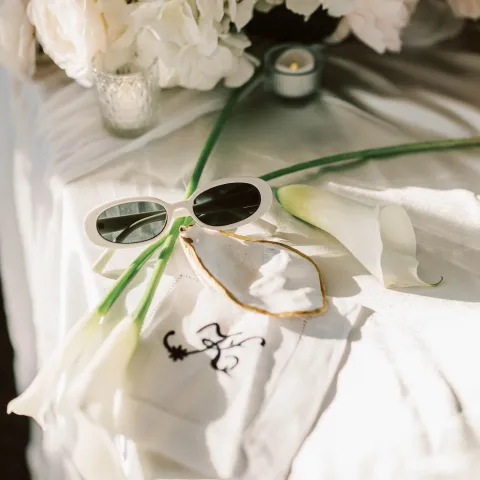 Table with white flowers, sunglasses, calla lilies, and a small candle.