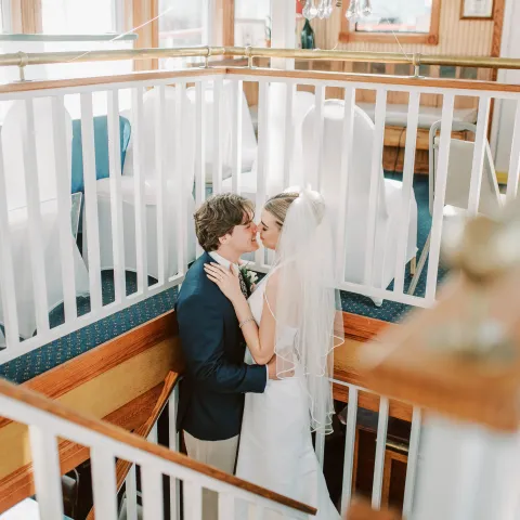 Bride and groom kissing on staircase in a warmly lit room.