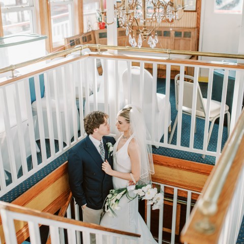 Bride and groom on staircase in elegant setting with chandelier.
