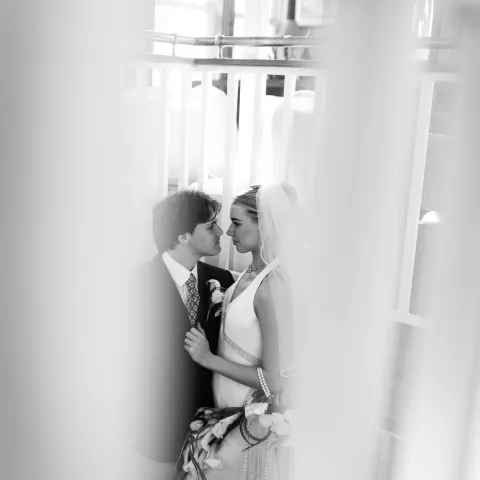 Bride and groom embrace on a staircase, framed by railings.