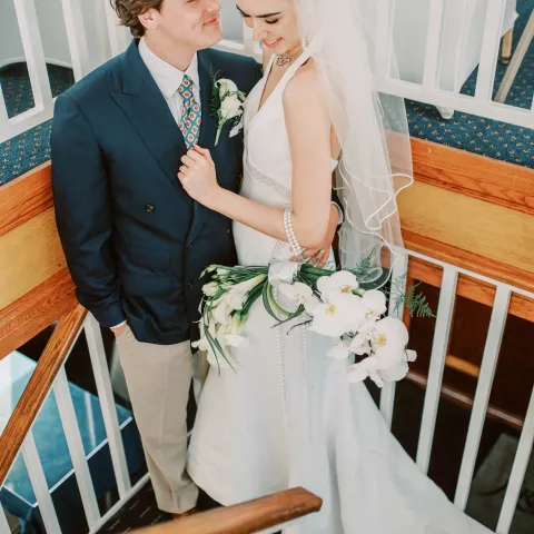 Bride and groom on staircase, she in white gown, he in blue suit.