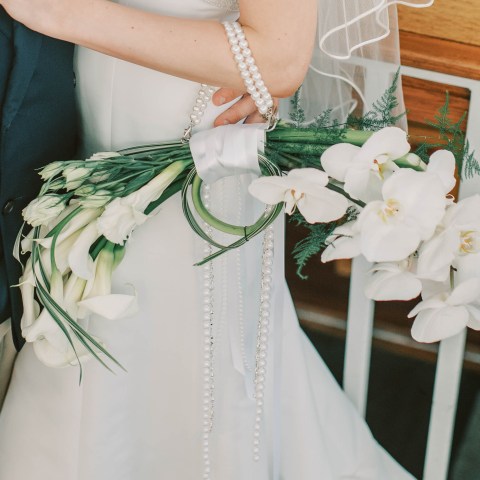 Bride holding white flower bouquet with greenery and pearl accents.