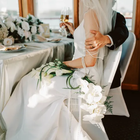 Bride in white dress sits with groom at a decorated table.