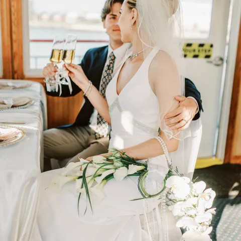Bride and groom sitting, toasting champagne, bride holding a bouquet.