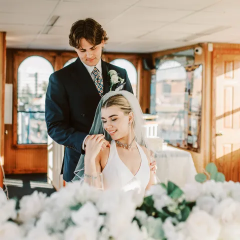 Bride and groom posing indoors, surrounded by white flowers.