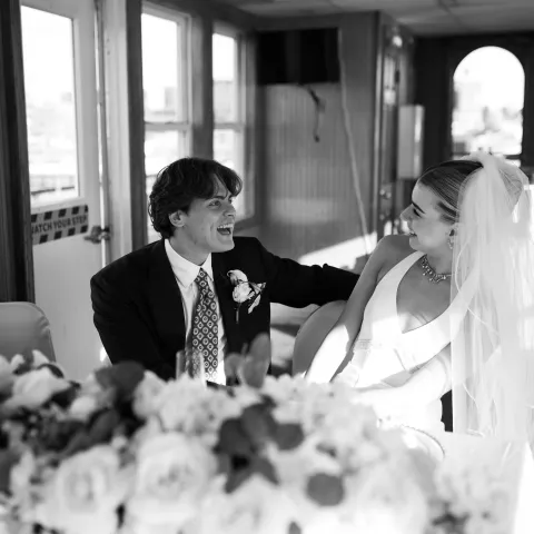 Bride and groom smiling at a table with flowers indoors.