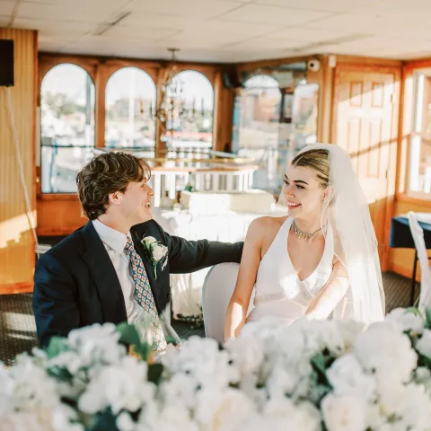 Bride and groom joyfully sitting together on a boat with floral decor.