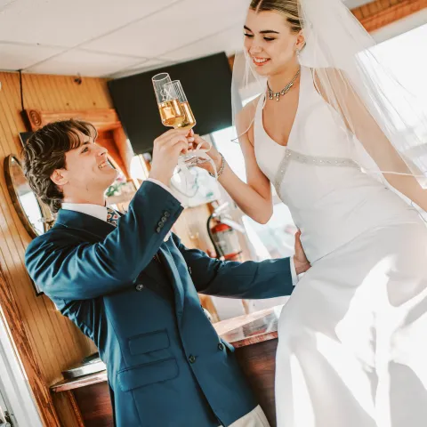 Couple in wedding attire exchanging a toast indoors.