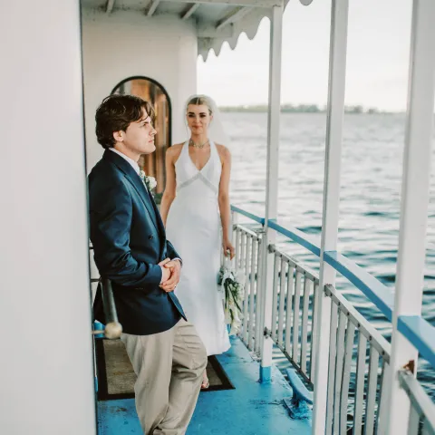 Bride and groom on a boat deck with railing and water view.