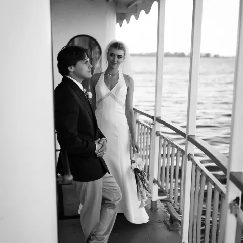 Bride and groom on boat deck, groom leaning against rail.