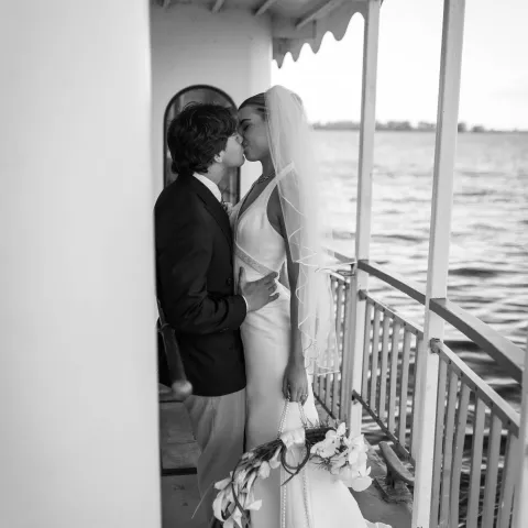 Bride and groom kissing on a boat near railing.