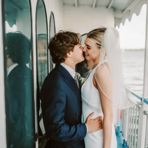 Bride and groom embracing on a boat deck facing each other.