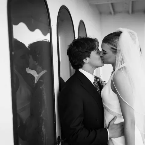 Bride and groom kissing on a boat, reflected in arched windows.