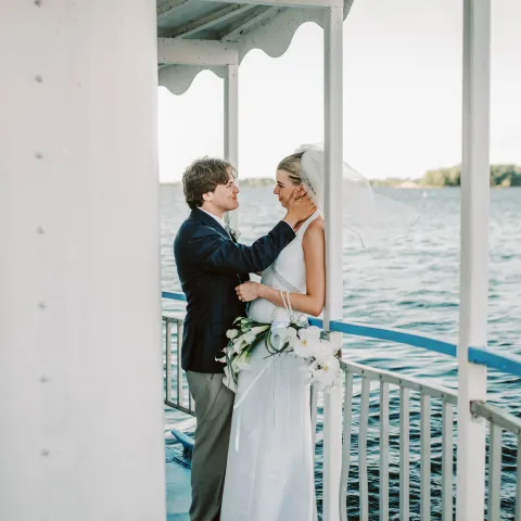 Bride and groom embracing on a boat deck over water.