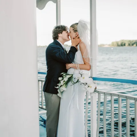 Bride and groom kissing on a boat, bride holding white flowers.