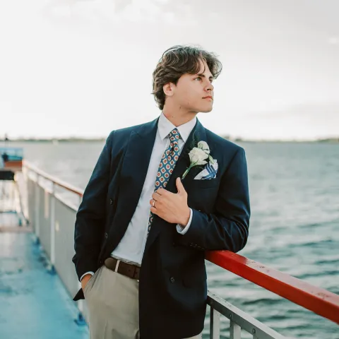Man in suit with boutonniere on boat deck overlooking the water.