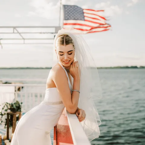 Bride in white dress posing on a boat with an American flag.