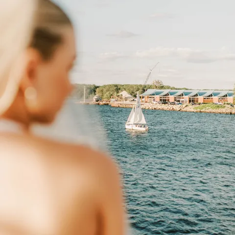 Close-up of a woman looking at a sailboat on a large body of water.