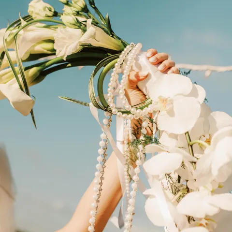 Hand holding a bouquet of white flowers against a blue sky.