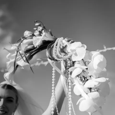 Bride holding bouquet with pearls and orchids against the sky.