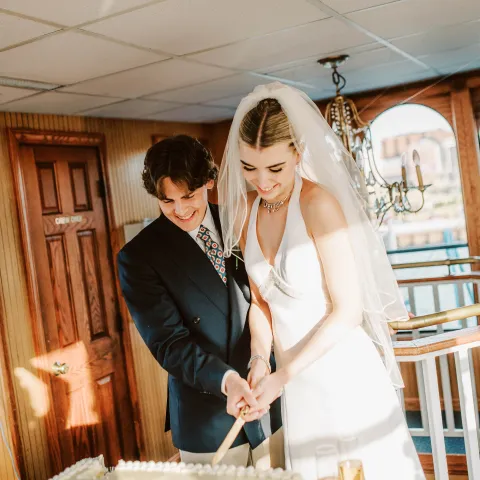 Bride and groom cutting a wedding cake together indoors.