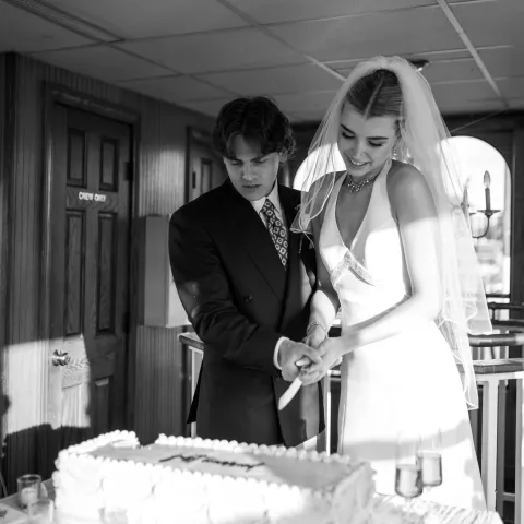 Bride and groom cutting wedding cake together indoors, black and white photo.