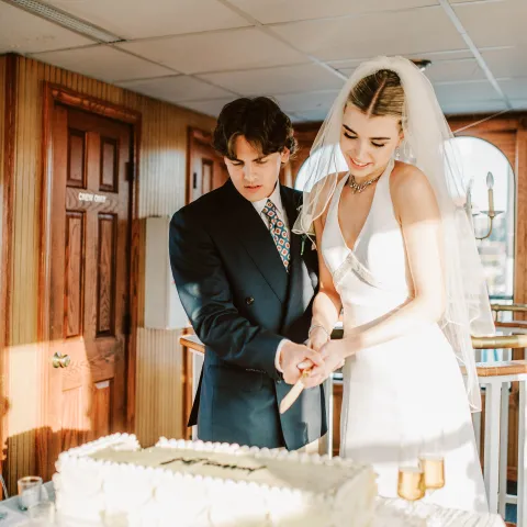 Bride and groom cutting a wedding cake together indoors.