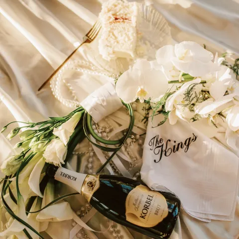 Champagne, flowers, pearls, and cake on satin with 'The King's' napkin.