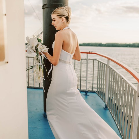 Woman in a wedding dress holding flowers on a boat deck.