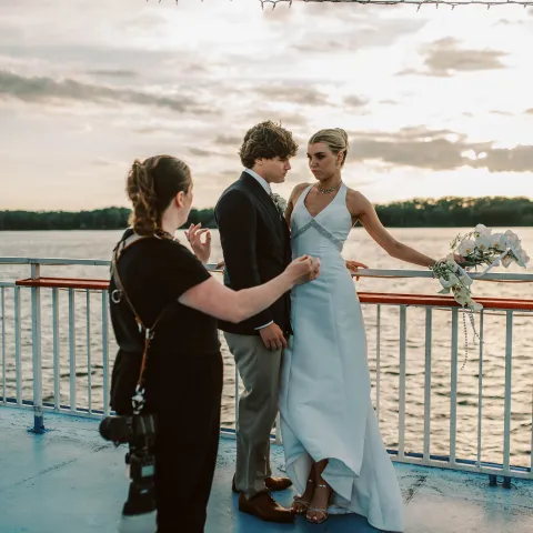 Couple poses for photos on a boat deck as photographer directs them.