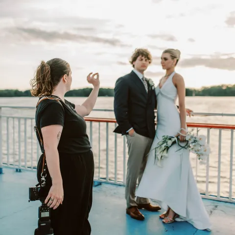 Photographer guides couple in wedding attire on a boat deck.