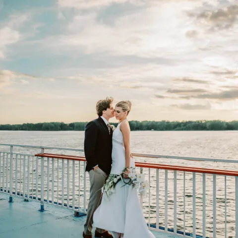 Bride and groom on a boat deck at sunset, near railing.