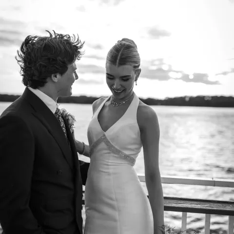 Couple smiling on a boat with lake and sunset in background.