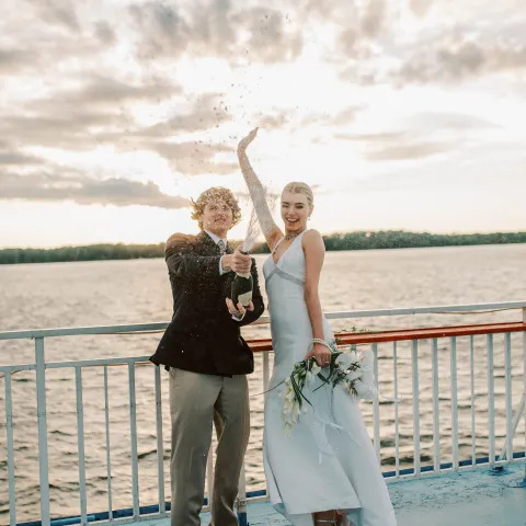 Couple celebrating with champagne on a boat deck at sunset.