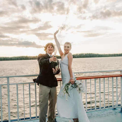 Bride and groom celebrate with champagne on a boat at sunset.