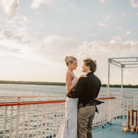 A couple in formal wear dancing on a boat deck at sunset.