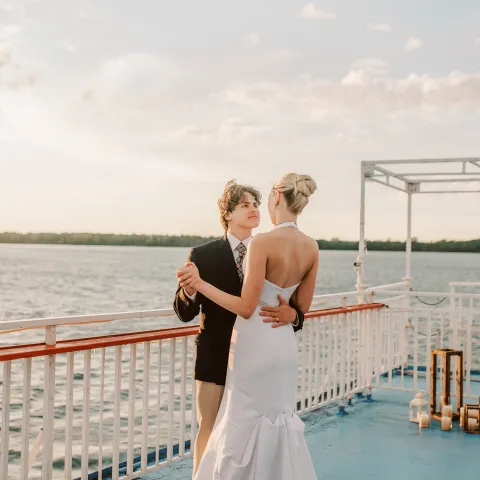 Couple dancing on a boat deck with water and sky in the background.